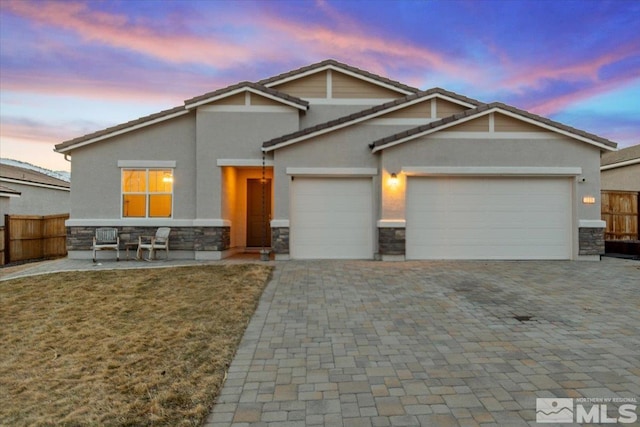 craftsman-style house featuring stone siding, decorative driveway, a garage, and fence