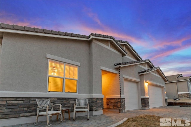 view of front of property featuring a tiled roof, a garage, stone siding, and stucco siding