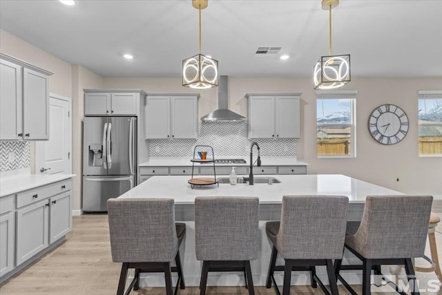 kitchen with gray cabinetry, wall chimney exhaust hood, and stainless steel refrigerator with ice dispenser