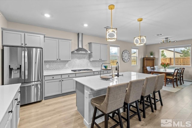 kitchen featuring backsplash, light countertops, stainless steel refrigerator with ice dispenser, gas stovetop, and wall chimney exhaust hood