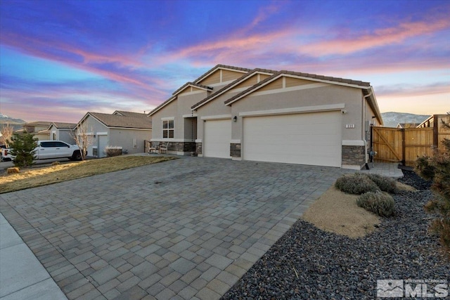 view of front of house with a tile roof, decorative driveway, stone siding, fence, and an attached garage