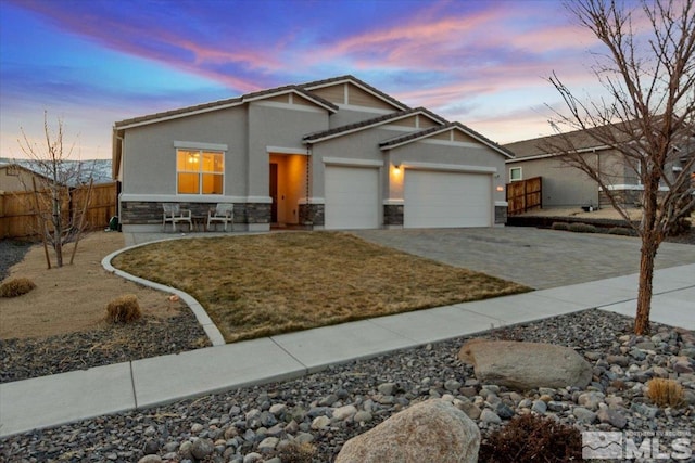 craftsman house with fence, stucco siding, driveway, stone siding, and an attached garage