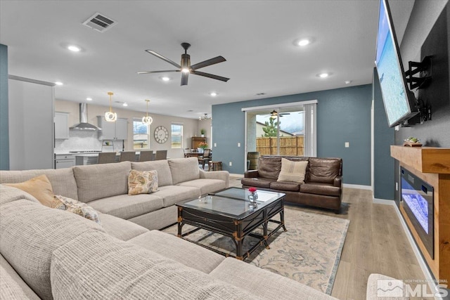 living area with visible vents, light wood-style flooring, a glass covered fireplace, recessed lighting, and ceiling fan