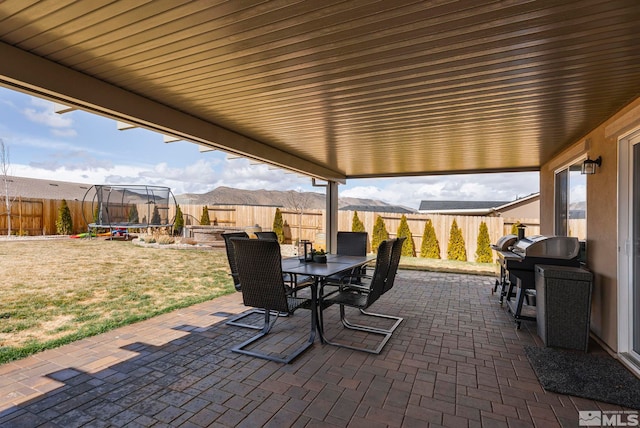 view of patio featuring outdoor dining area, a trampoline, a fenced backyard, and a mountain view