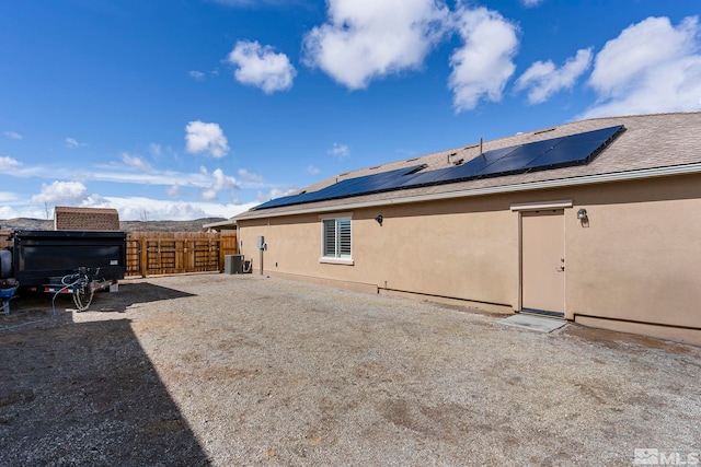 rear view of property featuring roof mounted solar panels, fence, central AC, and stucco siding