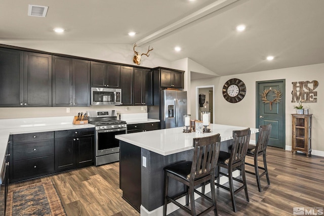 kitchen with visible vents, vaulted ceiling with beams, a breakfast bar area, appliances with stainless steel finishes, and dark wood-style floors