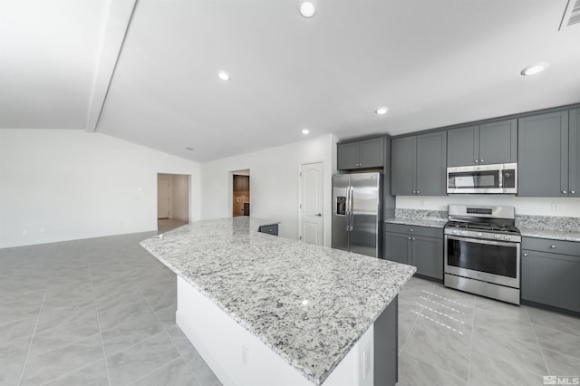 kitchen featuring a center island, vaulted ceiling, light stone counters, gray cabinets, and stainless steel appliances