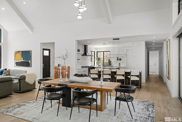 dining room with beam ceiling, recessed lighting, light wood finished floors, and a high ceiling