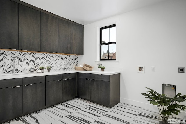 kitchen with modern cabinets, a sink, backsplash, light countertops, and baseboards