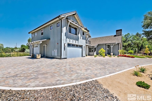 exterior space featuring decorative driveway, a garage, board and batten siding, and a chimney