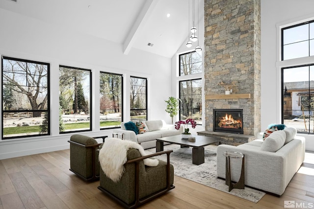 living area featuring beamed ceiling, visible vents, high vaulted ceiling, hardwood / wood-style floors, and a stone fireplace