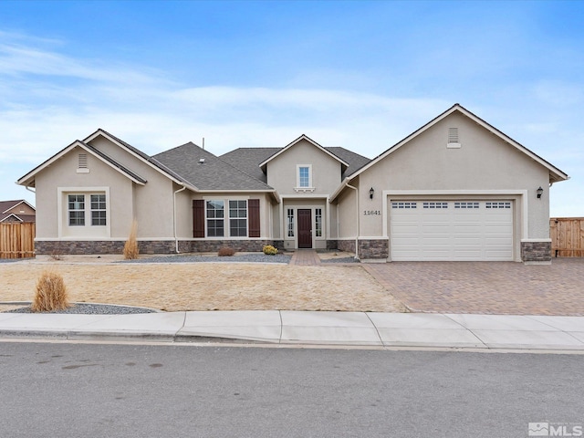 view of front of home featuring stone siding, stucco siding, decorative driveway, and fence