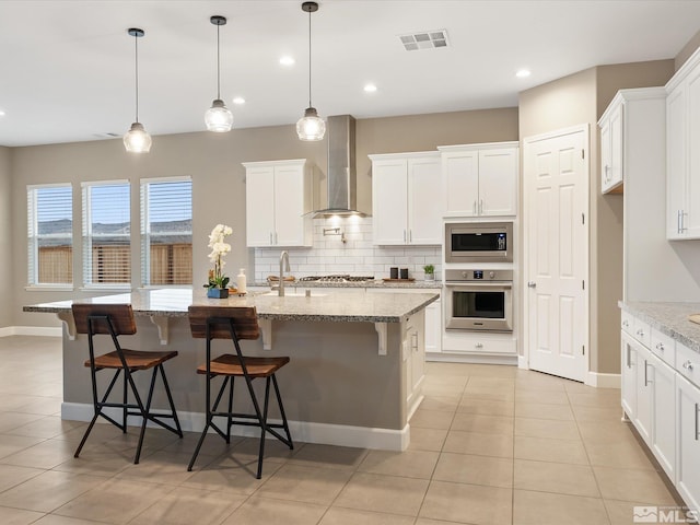 kitchen featuring light tile patterned floors, appliances with stainless steel finishes, white cabinetry, wall chimney exhaust hood, and tasteful backsplash