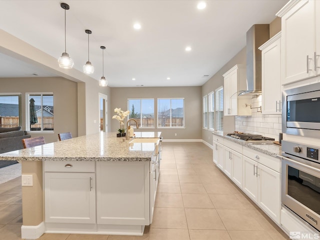 kitchen with light tile patterned floors, a sink, stainless steel appliances, wall chimney exhaust hood, and tasteful backsplash