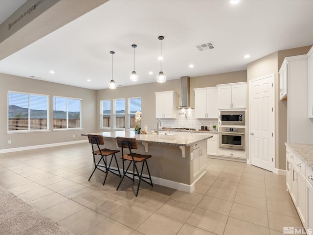 kitchen featuring visible vents, a sink, decorative backsplash, appliances with stainless steel finishes, and wall chimney exhaust hood