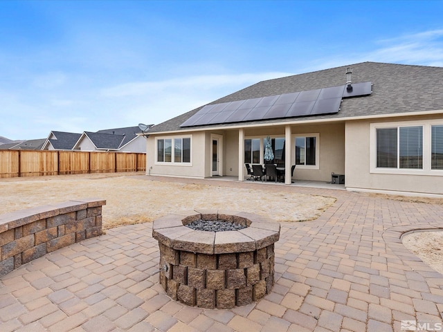 rear view of house featuring roof with shingles, a fenced backyard, stucco siding, a fire pit, and a patio area