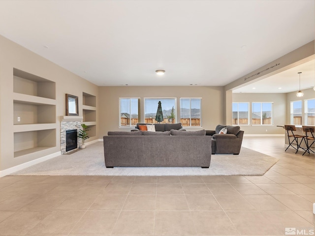 living area featuring light tile patterned floors, baseboards, built in shelves, and a stone fireplace