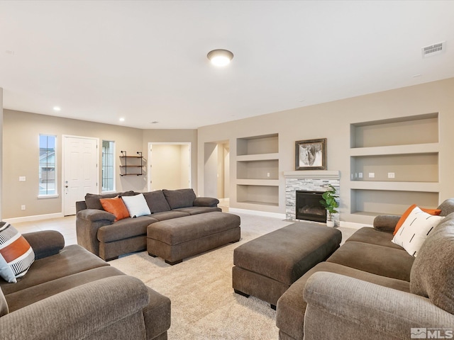 living room featuring visible vents, built in shelves, light carpet, a fireplace, and baseboards