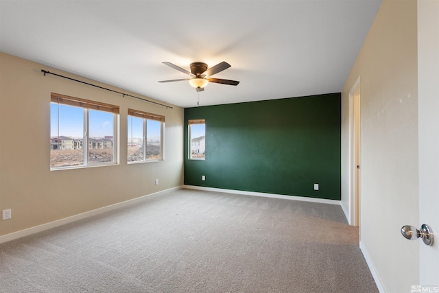 carpeted empty room with baseboards, an accent wall, and a ceiling fan