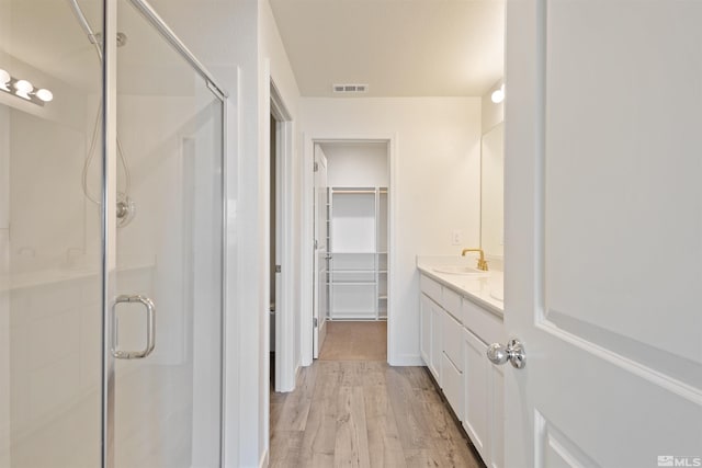 full bathroom featuring vanity, wood finished floors, visible vents, a shower stall, and a walk in closet