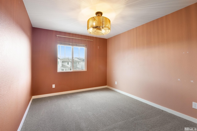 carpeted empty room featuring a notable chandelier and baseboards