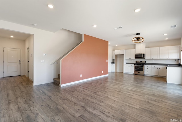 unfurnished living room featuring stairway, light wood-style flooring, visible vents, and a sink