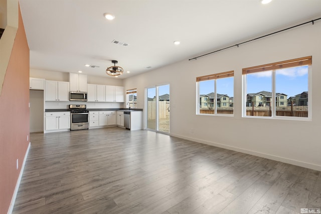 unfurnished living room with visible vents, baseboards, a healthy amount of sunlight, and wood finished floors