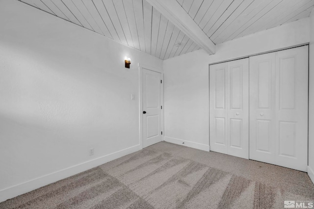 unfurnished bedroom featuring beamed ceiling, a closet, carpet floors, baseboards, and wood ceiling