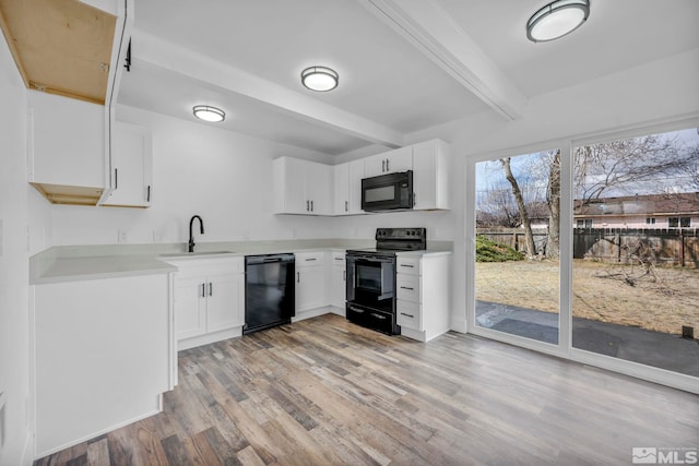 kitchen featuring beam ceiling, light wood-style flooring, a sink, black appliances, and light countertops