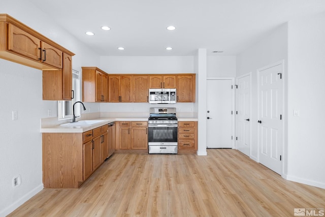 kitchen with appliances with stainless steel finishes, light wood-type flooring, light countertops, and a sink