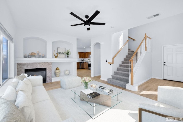 living room with visible vents, stairway, light wood finished floors, baseboards, and ceiling fan