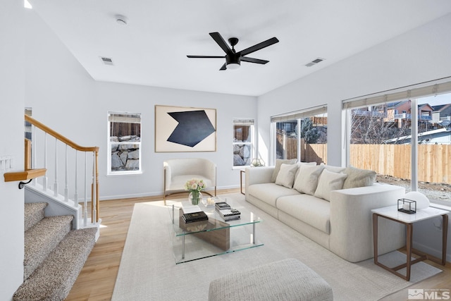 living area featuring baseboards, visible vents, light wood finished floors, ceiling fan, and stairs