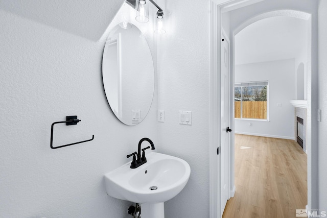 bathroom featuring a glass covered fireplace, wood finished floors, baseboards, and a sink