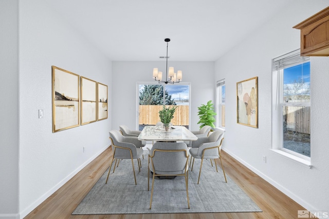 dining room with baseboards, a notable chandelier, and light wood finished floors