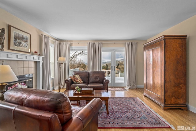 living room with a tiled fireplace, plenty of natural light, baseboards, and light wood-type flooring