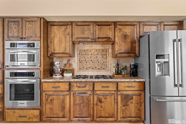 kitchen featuring stone countertops, backsplash, appliances with stainless steel finishes, and brown cabinetry