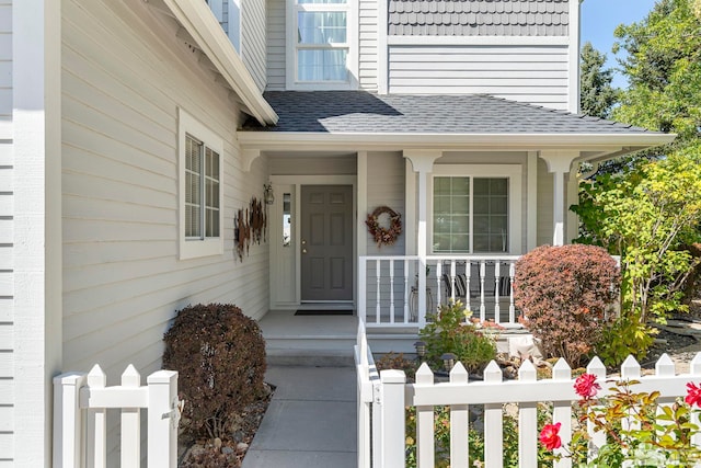 view of exterior entry featuring a porch, roof with shingles, and fence