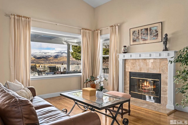 living area featuring a tile fireplace, baseboards, and wood finished floors