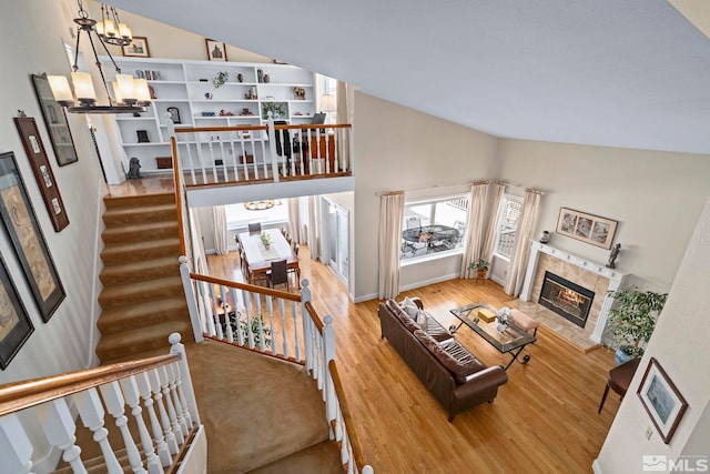 living room featuring a notable chandelier, wood finished floors, a fireplace, and vaulted ceiling