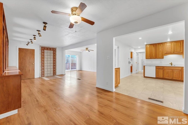 unfurnished living room featuring a ceiling fan, visible vents, a sink, light wood-style floors, and a textured ceiling