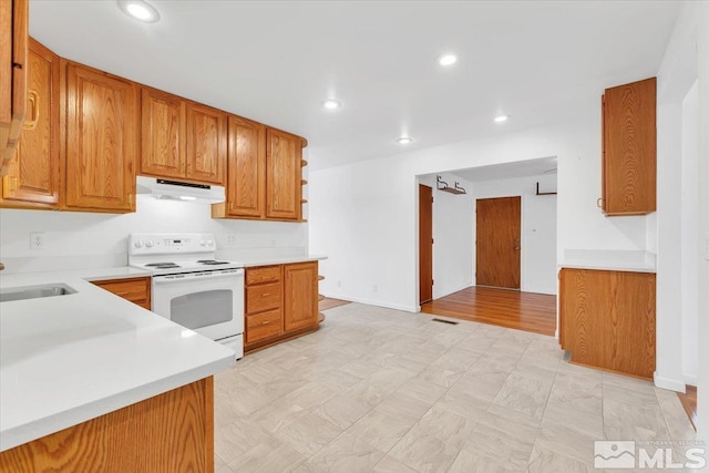 kitchen with under cabinet range hood, light countertops, brown cabinets, white electric range, and a sink