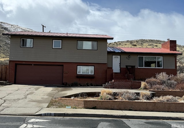 tri-level home featuring an attached garage, a chimney, brick siding, and metal roof