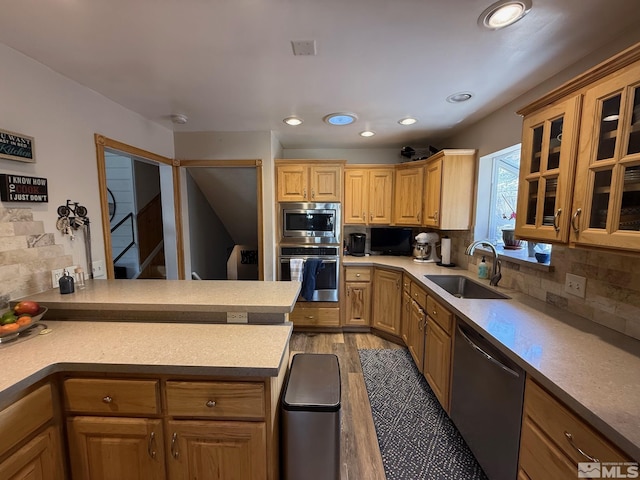 kitchen featuring wood finished floors, a sink, decorative backsplash, stainless steel appliances, and glass insert cabinets