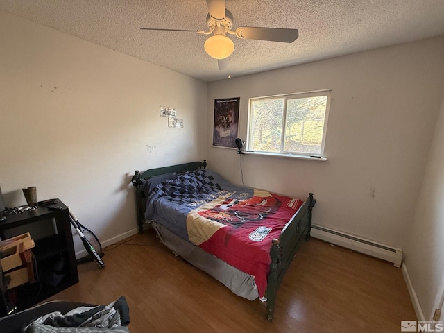 bedroom with a ceiling fan, a baseboard heating unit, a textured ceiling, wood finished floors, and baseboards