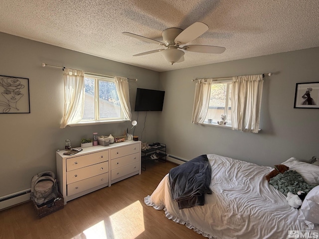 bedroom featuring a ceiling fan, multiple windows, wood finished floors, and a baseboard heating unit