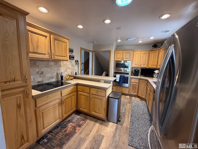 kitchen with light wood finished floors, tasteful backsplash, stainless steel appliances, a peninsula, and light countertops