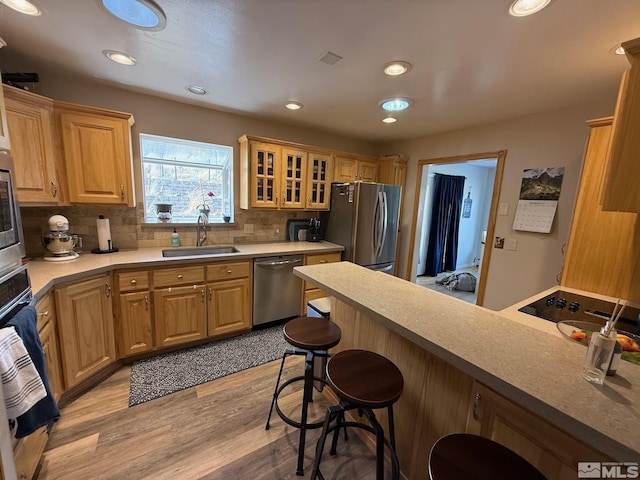 kitchen with a breakfast bar, a sink, glass insert cabinets, appliances with stainless steel finishes, and backsplash