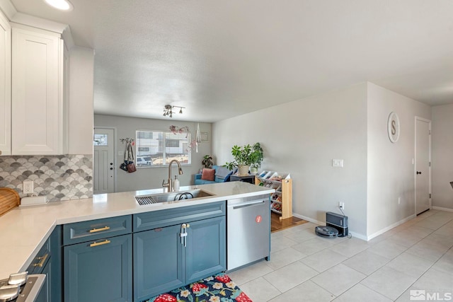 kitchen with a sink, backsplash, light countertops, a peninsula, and stainless steel dishwasher