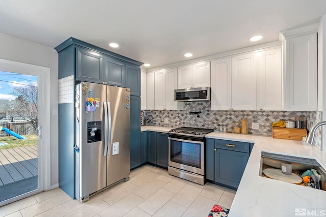 kitchen with backsplash, light tile patterned floors, light stone counters, appliances with stainless steel finishes, and a sink