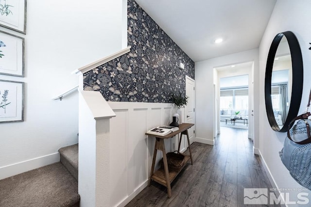 hallway featuring a wainscoted wall, dark wood-type flooring, stairway, wallpapered walls, and baseboards